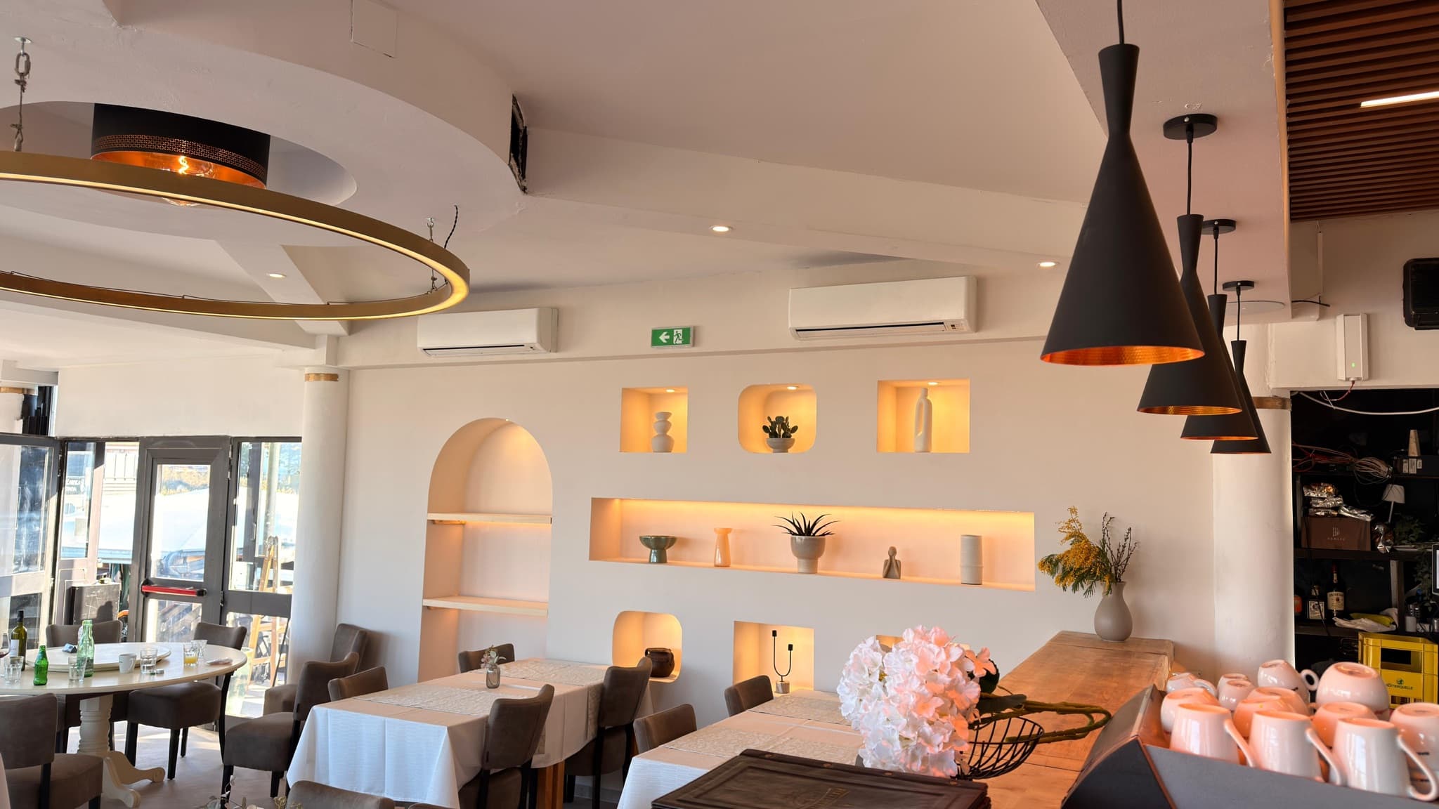 Interijer restorana s prstenastim lusterom i osvijetljenim zidnim nišama.